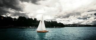 Image of a sailboat sailing on a lake, with cloudy weather above.